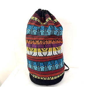 May include: A colourful drawstring bag with a black base and top. The bag features a vibrant woven pattern with blue, red, yellow, and white geometric designs. The bag is made of a sturdy fabric and has a black drawstring closure.