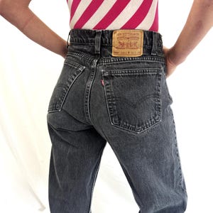 May include: High-waisted black denim jeans featuring a tan leather patch on the back waistband with the text Levi Strauss & Co. 550 32 34, a small red tab on the back pocket, and a classic five-pocket design with visible stitching and metal rivets.