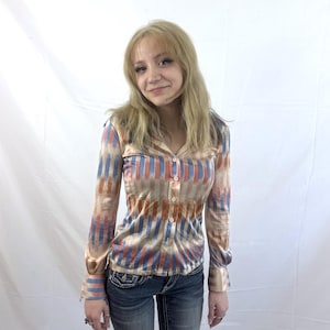May include: A long-sleeved button-down shirt featuring a vertical striped pattern in shades of blue, orange, and beige. The shirt has a collared neckline, a front button placket with white buttons, and fitted cuffs at the end of each sleeve.