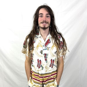 May include: A white short-sleeved button-down shirt with a colourful pattern of red, blue, and yellow. The pattern features a repeated design of stylised shoes and other objects.