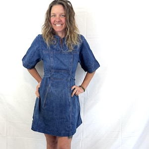 May include: A woman wearing a blue denim dress with a short sleeve and a fitted waist. The dress has a V-neckline and a slightly flared skirt.