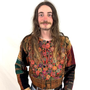 May include: A long-sleeved jacket featuring a vibrant, multi-colored floral embroidery pattern on the front chest. The garment is constructed from various patchwork fabric panels in shades of brown, black, green, and red, with a button-down front.