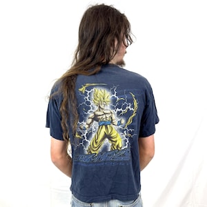 May include: A navy blue t-shirt with a graphic print of a yellow-haired anime character with a blue belt and a yellow and blue outfit. The character is surrounded by lightning bolts.