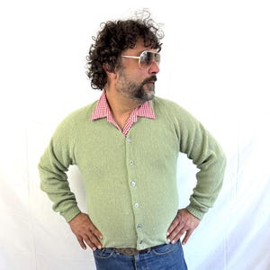 Op de afbeelding: Een lichtgroene cardigan met knopen en lange mouwen. De cardigan is gemaakt van een zachte, textuurrijke stof.