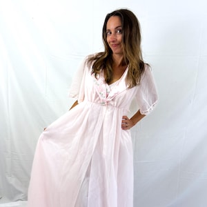 May include: A light pink vintage robe with a matching nightgown. The robe features short sleeves with lace trim and a floral embroidered detail on the bodice. The nightgown is visible underneath. The fabric appears to be a sheer, lightweight material.