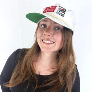 May include: White baseball cap with a green brim featuring the text "Designed for Microsoft Windows 95" and "COMPAQ". The cap has a rope detail along the brim and a red and white patch.