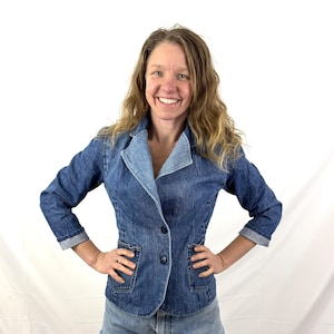 Peut inclure: Un blazer en jean avec un revers et des poignets bleu clair. La veste a deux poches avant et une fermeture à un seul bouton. Les manches sont retroussées. Le blazer est associé à un short en jean.