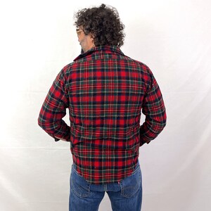 May include: A red, green, and black plaid flannel shirt with long sleeves. The shirt is buttoned up and the collar is turned up.