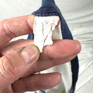 May include: A close-up of a navy blue garment with a white interior and a white, textured fabric detail. The garment has a navy blue trim and a white stitched seam.