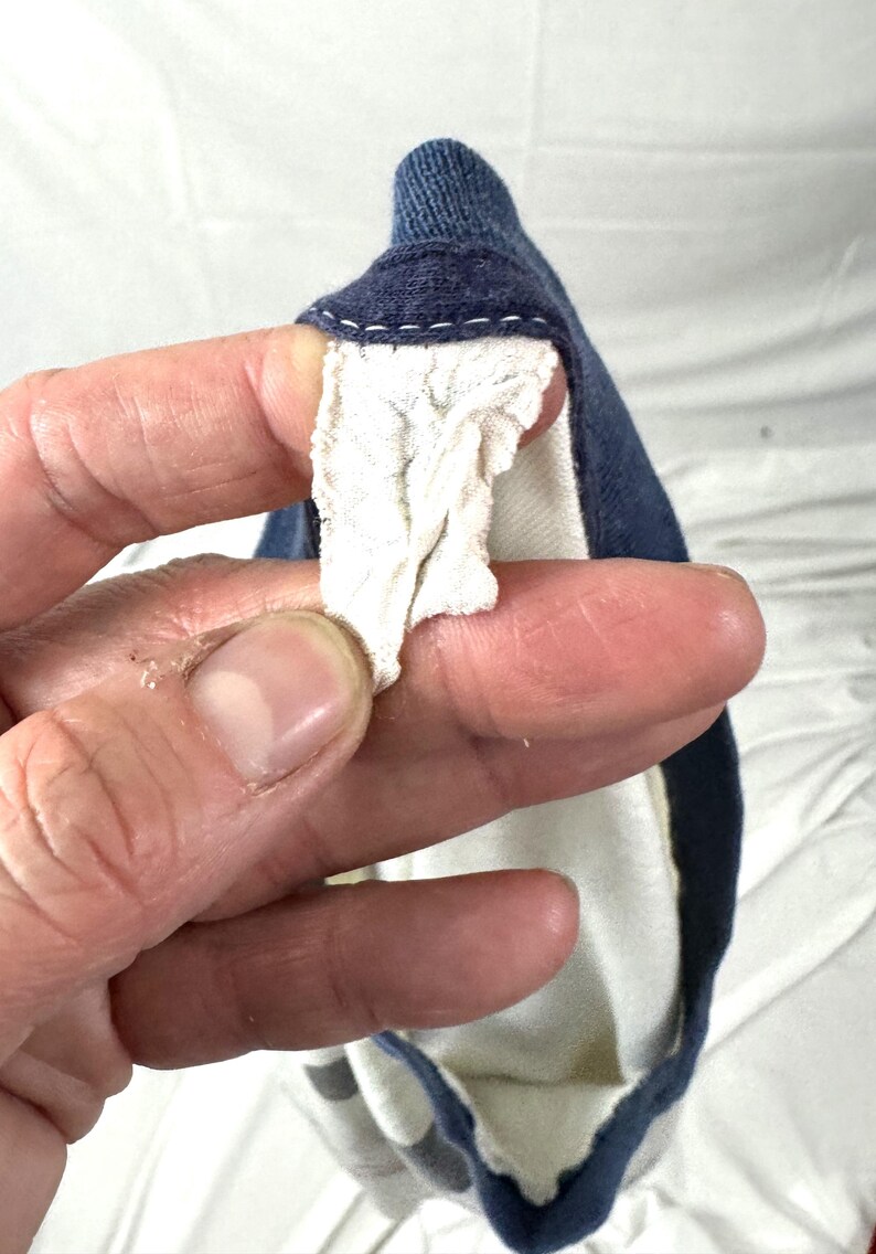 May include: A close-up of a navy blue garment with a white interior and a white, textured fabric detail. The garment has a navy blue trim and a white stitched seam.