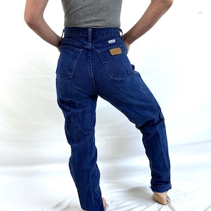 K&ouml;nnte beinhalten: Eine blaue Jeans mit hoher Taille und einem braunen Leder-Wrangler-Etikett auf der Ges&auml;&szlig;tasche.