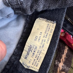Puede incluir: Primer plano de unos vaqueros Wrangler de mezclilla oscura. La etiqueta dice "Wrangler Brand" e incluye la talla 7 y la longitud 34. La etiqueta tambi&eacute;n incluye instrucciones de lavado y est&aacute; fabricada en EE. UU.