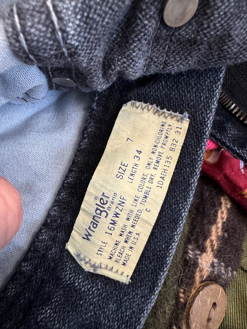 Puede incluir: Primer plano de unos vaqueros Wrangler de mezclilla oscura. La etiqueta dice "Wrangler Brand" e incluye la talla 7 y la longitud 34. La etiqueta tambi&eacute;n incluye instrucciones de lavado y est&aacute; fabricada en EE. UU.