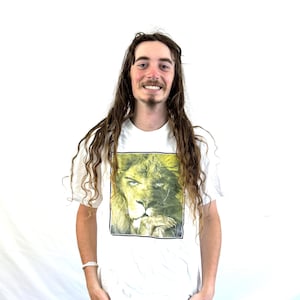 May include: A white t-shirt with a graphic of a lion's face. The lion has a yellow mane and green eyes. The lion is looking directly at the viewer.