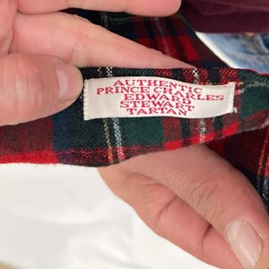 May include: Close-up of a red and green plaid fabric with a white label that reads "Authentic Prince Charles Edward Stewart Tartan".