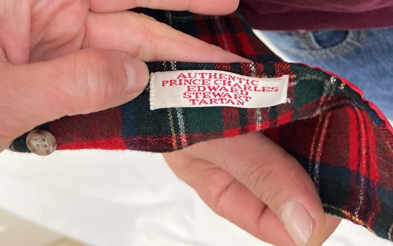 May include: Close-up of a red and green plaid fabric with a white label that reads "Authentic Prince Charles Edward Stewart Tartan".