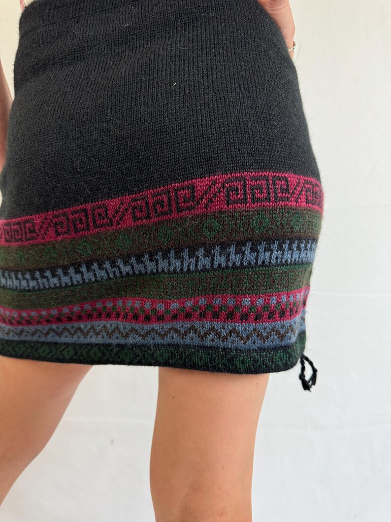 May include: Black knitted skirt with a colorful geometric pattern at the hem. The skirt is made of a soft, warm material and has a drawstring at the side.