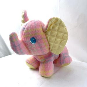May include: A plush elephant toy in a pink, yellow, and blue plaid pattern. The elephant has a blue eye, yellow quilted ears, and yellow feet. This soft toy is suitable for children.