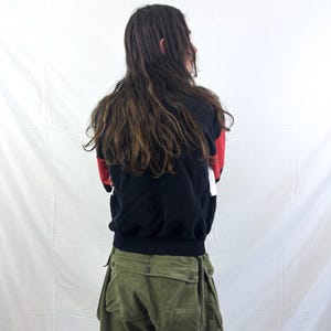 May include: A person wearing a black, red, and white color block sweatshirt and olive green cargo pants. The sweatshirt has a black base with red and white accents. The cargo pants have multiple pockets and a button closure.