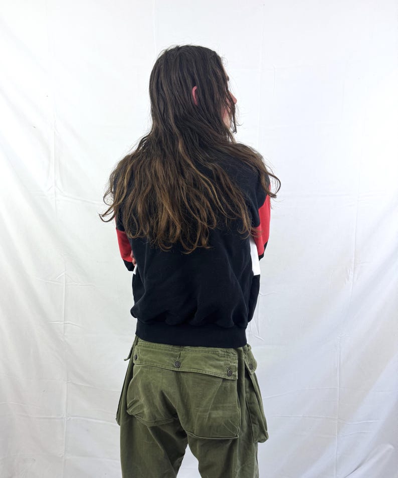 May include: A person wearing a black, red, and white color block sweatshirt and olive green cargo pants. The sweatshirt has a black base with red and white accents. The cargo pants have multiple pockets and a button closure.