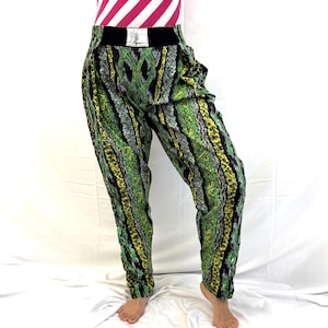 May include: Green, yellow, and black patterned pants with a black waistband. The pants have a unique design with vertical stripes and geometric shapes. The model is also wearing a pink and white striped top.