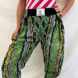 May include: Green, yellow, and black patterned pants with a wide black waistband. The pants feature a repeating geometric design. The waistband has a tag with text. The top is a pink and white striped tank top.