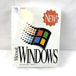 Può includere: Una scatola bianca di Microsoft Windows Sistema Operativo Versione 3.1 con il logo Windows al centro. Il logo presenta un design quadrato colorato. Una stella rossa con la scritta "NEW!" si trova in alto a destra.