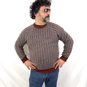 Puede incluir: Un su&eacute;ter con estampado marr&oacute;n y blanco con cuello redondo y mangas largas. El su&eacute;ter tiene un dise&ntilde;o geom&eacute;trico y se usa con jeans azules. Los pu&ntilde;os y el dobladillo son de color marr&oacute;n oscuro.