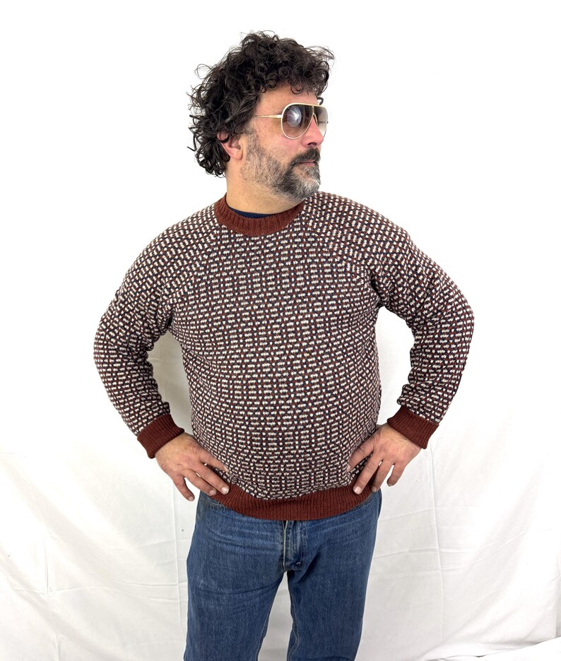 Puede incluir: Un su&eacute;ter con estampado marr&oacute;n y blanco con cuello redondo y mangas largas. El su&eacute;ter tiene un dise&ntilde;o geom&eacute;trico y se usa con jeans azules. Los pu&ntilde;os y el dobladillo son de color marr&oacute;n oscuro.