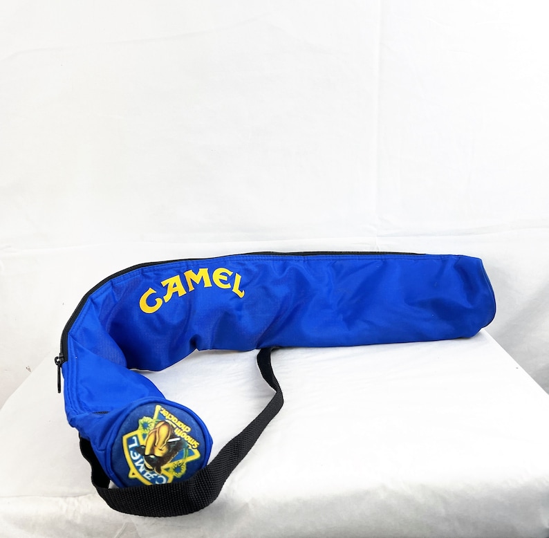 May include: A bright blue cylindrical carrying case with a black zipper and a black shoulder strap. The word CAMEL is printed in yellow on the side. A circular end cap features a yellow and blue logo with a camel graphic and the text Smooth character.