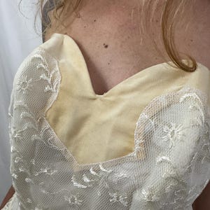 Puede incluir: Cuerpo de vestido sin tirantes color crema con escote coraz&oacute;n. El corpi&ntilde;o est&aacute; hecho de una tela suave de color amarillo claro, cubierta con delicado encaje blanco con motivos florales. El encaje se extiende sobre los hombros.