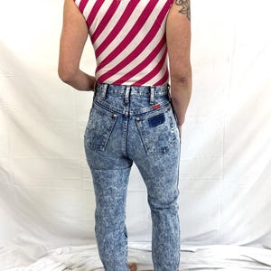 Puede incluir: Un body sin mangas con un estampado de rayas rosas y blancas combinado con unos vaqueros de mezclilla con lavado &aacute;cido. Los vaqueros tienen cintura alta y corte recto. El conjunto es de estilo vintage.