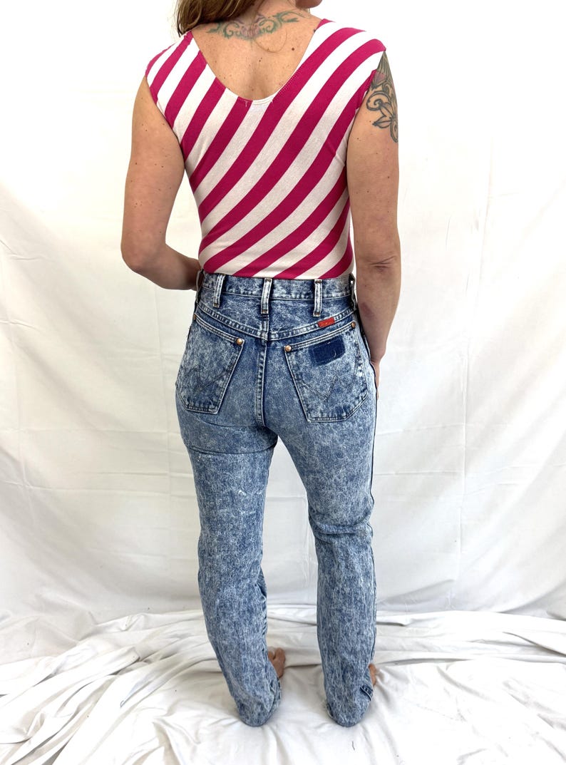 Puede incluir: Un body sin mangas con un estampado de rayas rosas y blancas combinado con unos vaqueros de mezclilla con lavado &aacute;cido. Los vaqueros tienen cintura alta y corte recto. El conjunto es de estilo vintage.