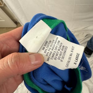 Puede incluir: Una camiseta azul y verde de manga larga con una etiqueta blanca. La etiqueta incluye el texto "RN 16490", "50% COTTON", "50% POLYESTER" y "X-LARGE". La camiseta est&aacute; hecha de una mezcla de algod&oacute;n y poli&eacute;ster.