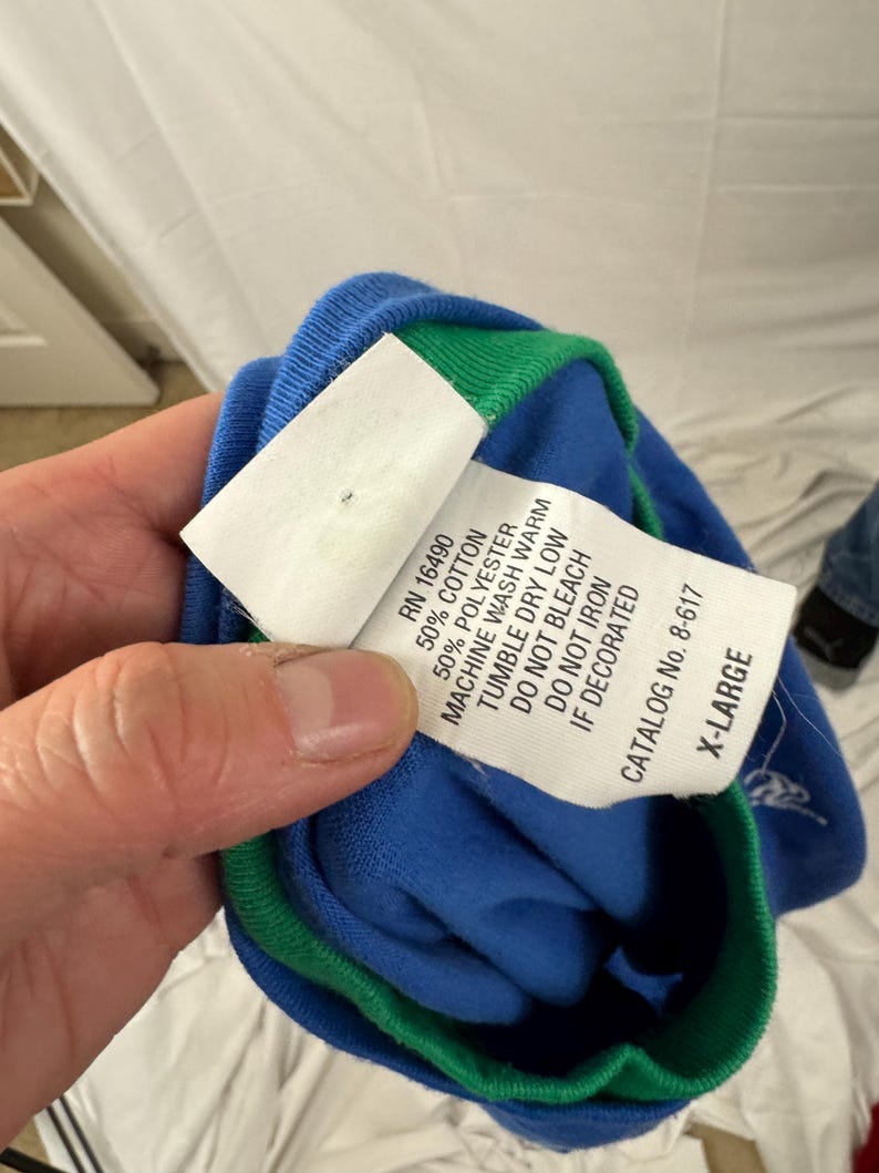 Puede incluir: Una camiseta azul y verde de manga larga con una etiqueta blanca. La etiqueta incluye el texto "RN 16490", "50% COTTON", "50% POLYESTER" y "X-LARGE". La camiseta est&aacute; hecha de una mezcla de algod&oacute;n y poli&eacute;ster.