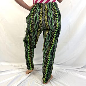 May include: Green, black, and yellow patterned pants. The pants have a snake-like design and a loose fit. The person in the image is wearing a pink and white striped top.