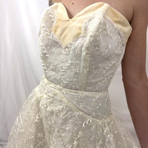 Puede incluir: Vestido vintage marfil sin tirantes con escote coraz&oacute;n. El corpi&ntilde;o presenta un ribete de terciopelo crema y est&aacute; cubierto con delicado encaje floral. La falda se ensancha, creando una silueta cl&aacute;sica.