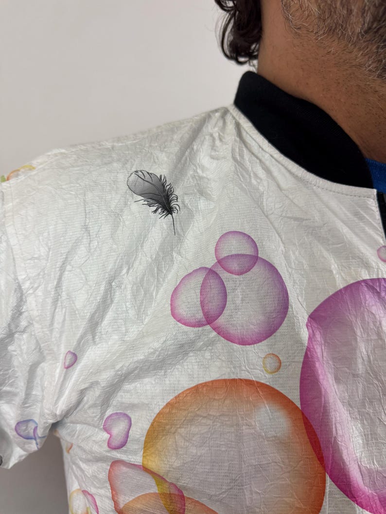 May include: White bomber jacket with a black collar and a feather and bubble design. The jacket features colorful bubbles in orange, pink, and purple. The feather is black and grey.