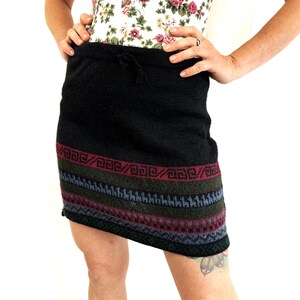 May include: Black knitted skirt with a colorful geometric pattern at the hem. The skirt has a drawstring waist.