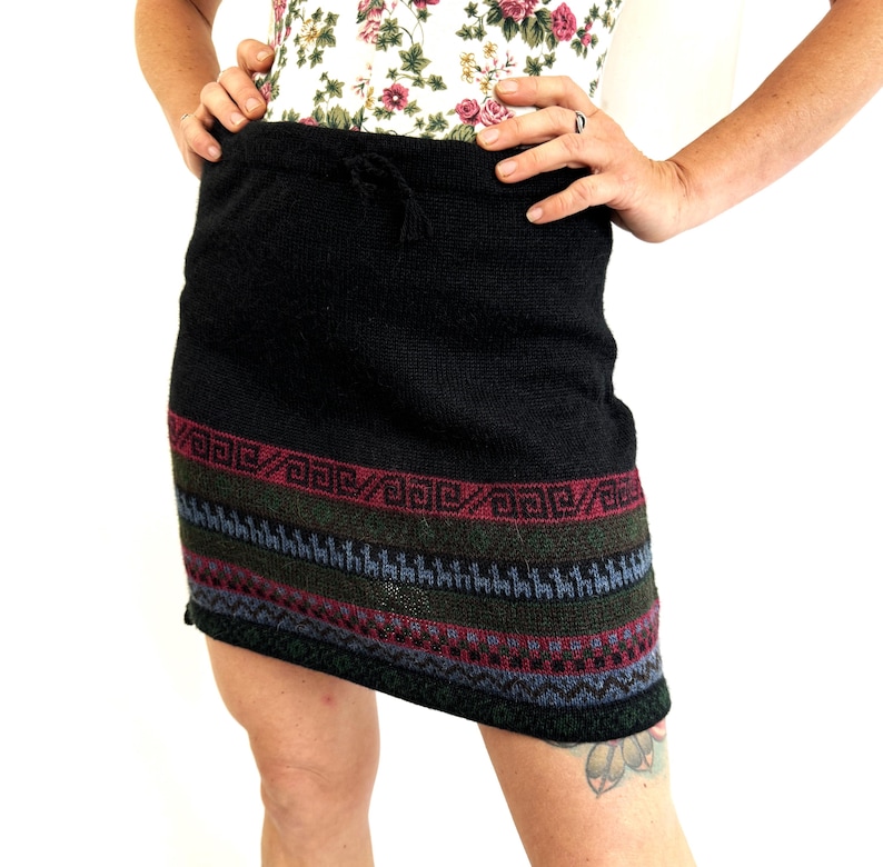 May include: Black knitted skirt with a colorful geometric pattern at the hem. The skirt has a drawstring waist.