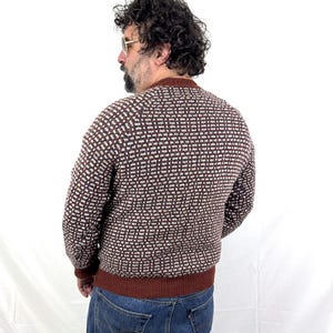 Puede incluir: Un su&eacute;ter marr&oacute;n y blanco estampado con cuello y pu&ntilde;os marrones acanalados. El su&eacute;ter tiene un dise&ntilde;o geom&eacute;trico y se usa con jeans azules. La persona lleva gafas de sol.