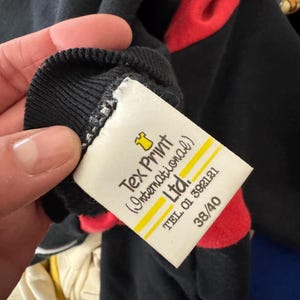 May include: Black long-sleeve shirt with red shoulder accents. The shirt has a ribbed collar and a tag that reads "Tex Print (International) Ltd." with a phone number and size 38/40.