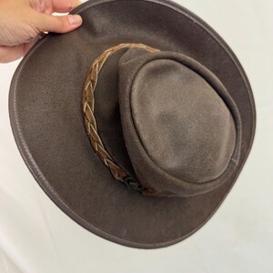 Puede incluir: Un sombrero de color marr&oacute;n oscuro con ala ancha y copa redondeada. El sombrero presenta una banda trenzada alrededor de la base de la copa, de un tono marr&oacute;n m&aacute;s claro. El material tiene un acabado mate y texturizado en toda la superficie.