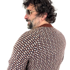 Puede incluir: Un su&eacute;ter estampado en marr&oacute;n, blanco y azul marino. El su&eacute;ter tiene cuello redondo y se usa con gafas de sol con montura dorada. La persona de la imagen tiene cabello oscuro rizado y barba.