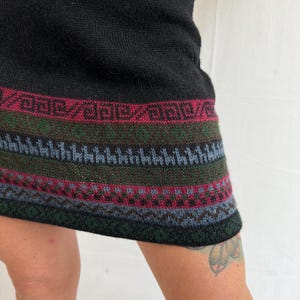 May include: Black knitted mini dress with a colorful geometric pattern around the hem.