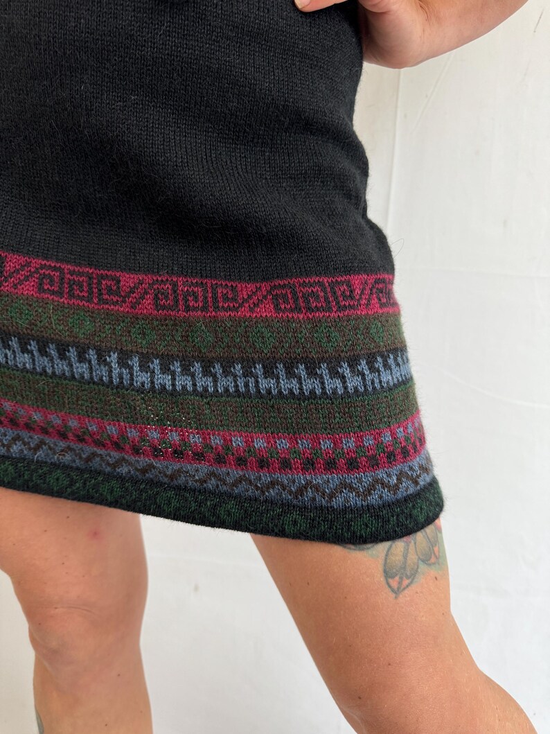 May include: Black knitted mini dress with a colorful geometric pattern around the hem.