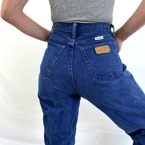 K&ouml;nnte beinhalten: Eine blaue Jeans mit hoher Taille und einem Wrangler-Lederpatch auf der Ges&auml;&szlig;tasche.