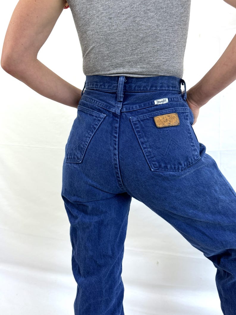 K&ouml;nnte beinhalten: Eine blaue Jeans mit hoher Taille und einem Wrangler-Lederpatch auf der Ges&auml;&szlig;tasche.