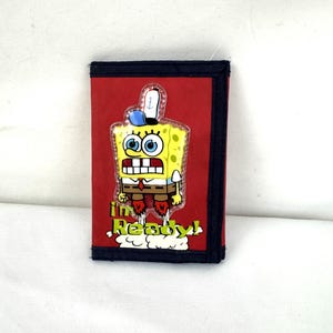 Könnte beinhalten: Ein rotes dreifach faltbares Portemonnaie mit schwarzem Rand, das eine Grafik der Zeichentrickfigur SpongeBob Schwammkopf mit einem blauen Hut zeigt. Unter der Figur ist der Text "I'm Ready!" in gelben Buchstaben aufgedruckt.