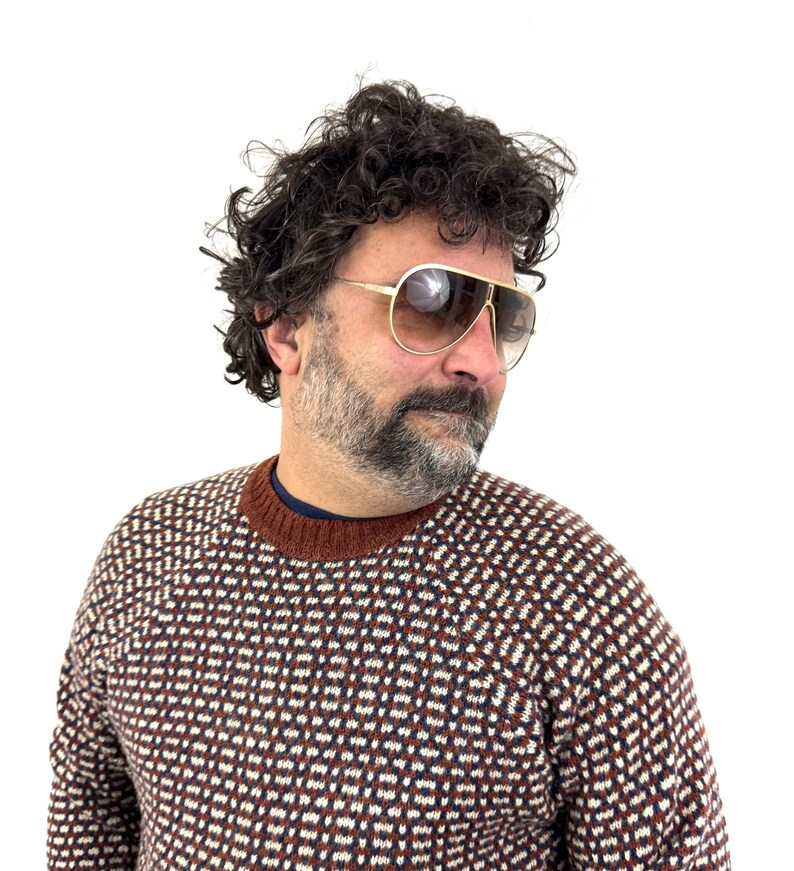 Puede incluir: Gafas de sol de aviador con montura dorada y lentes degradadas marrones. Las gafas de sol se llevan con un su&eacute;ter estampado en marr&oacute;n, blanco y azul marino. El su&eacute;ter tiene cuello redondo marr&oacute;n y una camiseta interior azul marino.